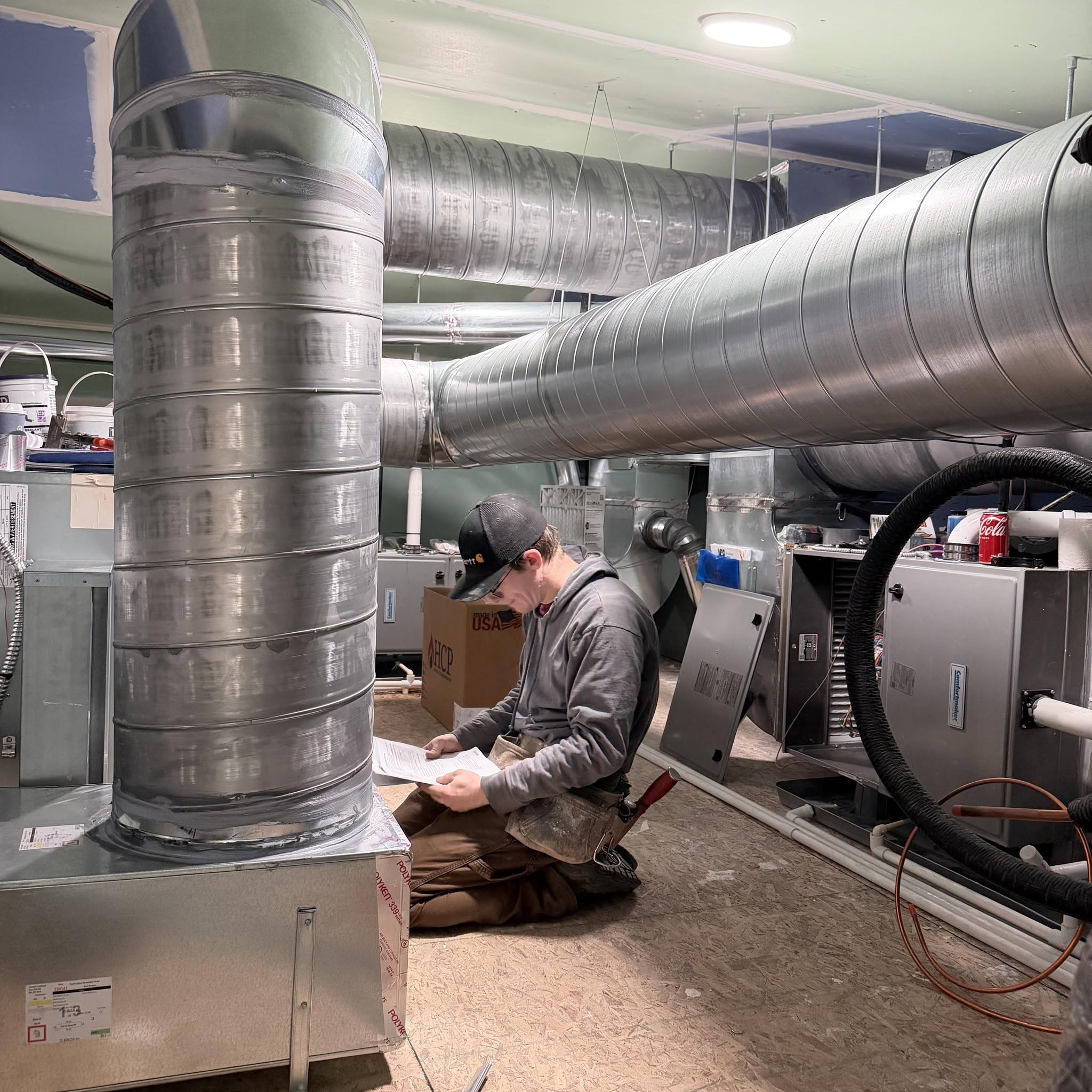 A Rockit HVAC technician checking the plans beside newly installed spiral trunk ductwork and equipment